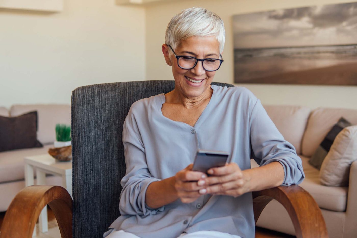 Smiling woman using smartphone while sitting in armchair.